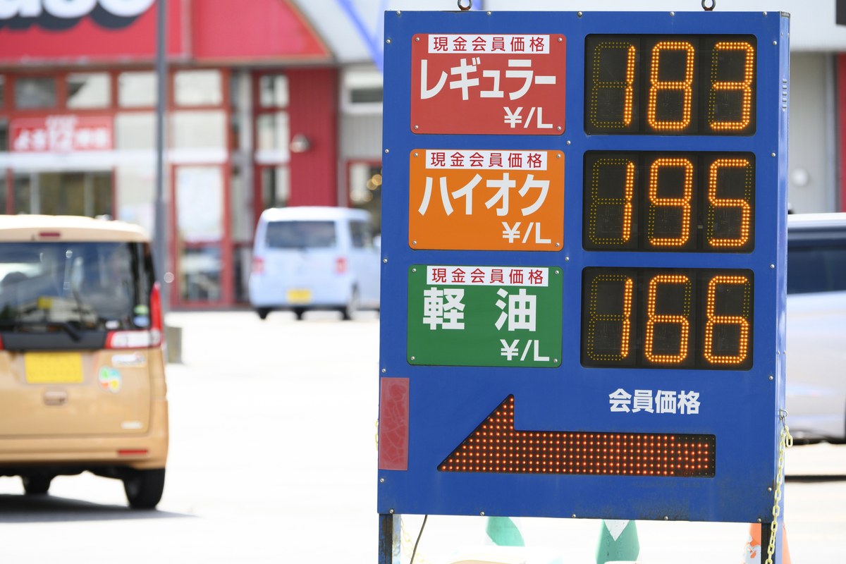 ガソリンスタンドの価格表示板と給油中のトラック
